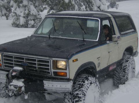 1986 Ford Bronco - A 1986 Ford Bronco navigates a snowy landscape with its large off-road tires, while another vehicle is visible in the background.