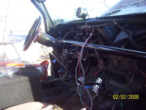 1978 Ford Bronco - The interior of a vehicle shows a complex and disorganized wiring harness, with a steering wheel and pedals in view.
