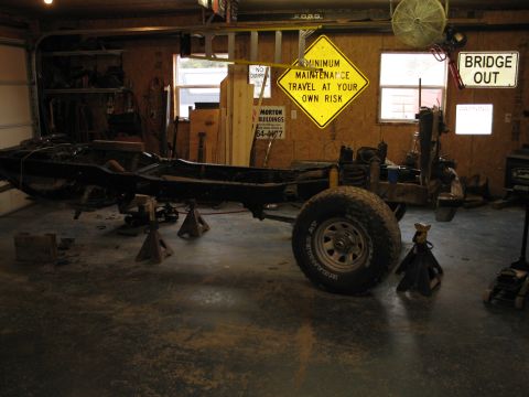 1995 Ford Bronco - The vehicle's frame is elevated on jack stands inside a garage, with one wheel attached.