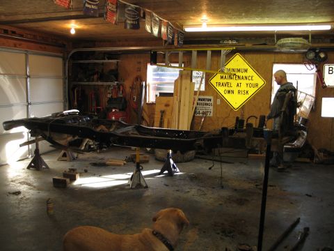 1995 Ford Bronco - A vehicle frame is elevated on jack stands inside a garage, with a dog lying on the floor in the foreground.