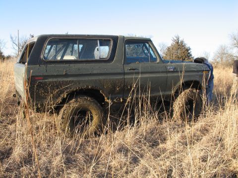 1995 Ford Bronco - A mud-splattered Ford Bronco sits in a field of dry grass under a clear blue sky.