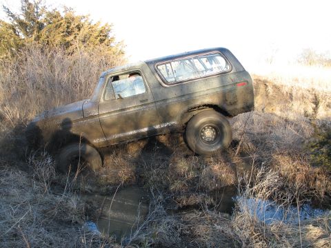 1995 Ford Bronco - This older model Ford Bronco is deeply stuck in a muddy ditch, with its front tires and lower body covered in mud.