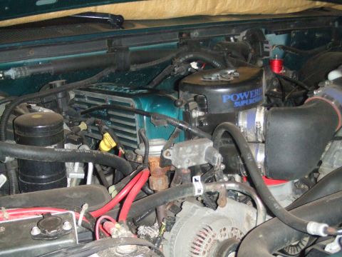 1996 Ford Bronco - Engine bay view of a green Ford truck showing a Powerdyne supercharger unit mounted at the front of the engine with a black intake tube and…
