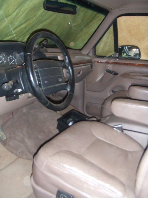 1996 Ford Bronco - Interior of a 1990s Ford truck shot from the passenger side, showing tan leather bucket seats, a tan door panel with woodgrain trim insert,…