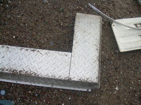 1991 Ford Bronco - A section of diamond plate metal trim is shown lying on the ground next to other vehicle parts.