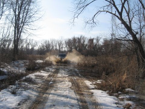 1996 Ford Bronco - A vehicle drives through a muddy, watery path surrounded by bare trees and dry brush.