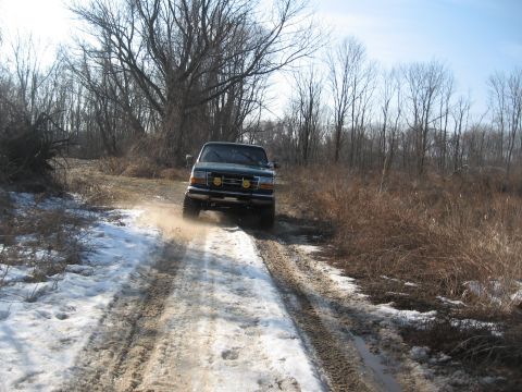 1996 Ford Bronco - 1996 Ford Bronco navigates a wintery dirt path, kicking up dust and snow.