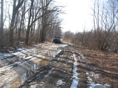 1996 Ford Bronco - A vehicle navigates a challenging off-road path with puddles and patches of snow.