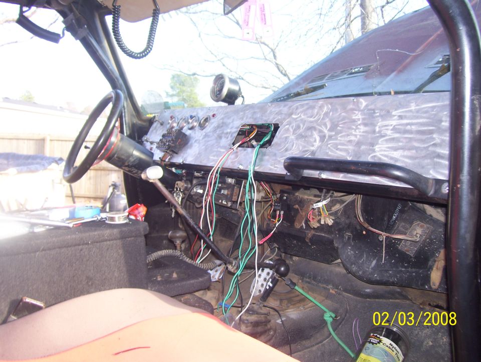 Vehicle interior showing dashboard, steering wheel, and exposed wiring. A roll cage is visible