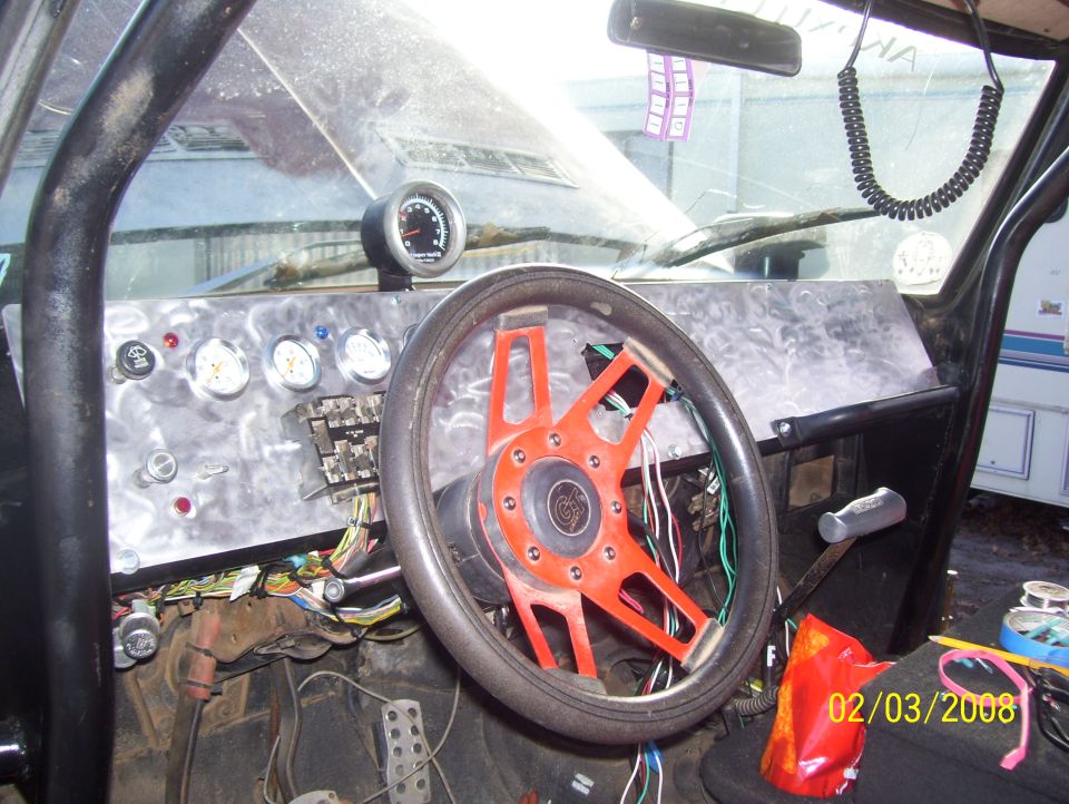 Custom dashboard with aftermarket gauges and an orange steering wheel. Wires are exposed under the dash