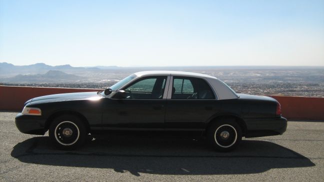 Black sedan with gray roof and black steel wheels parked at a scenic desert overlook, side view