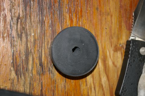 1986 Ford Bronco - A close-up view of a black rubber stopper with a hole in its center, resting on a wooden surface next to a knife.