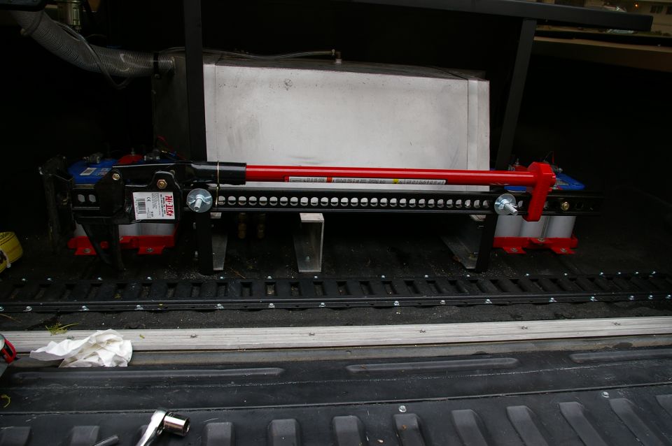 Hi-Lift jack with red handle and blue base, secured in a truck bed with tie-down rails