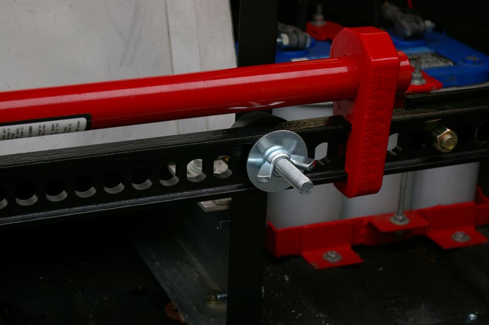Red hi-lift jack secured to black mounting rack with wingnut bolt