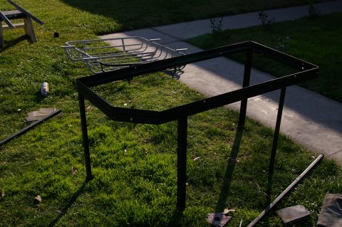 1986 Ford Bronco - A metal rack frame and basket are assembled on a grassy area next to a sidewalk.
