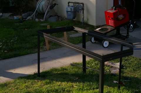 1986 Ford Bronco - A metal rack and a welding machine sit on a cart in a yard with a gas meter and hose reel visible.