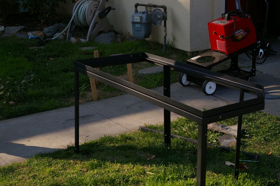 Black metal rack with a red Lincoln welding machine on a cart in a grassy yard
