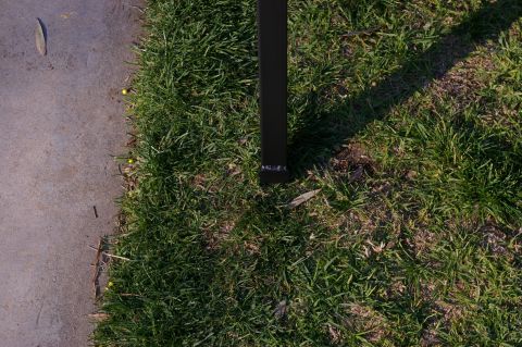 1986 Ford Bronco - A black metal post stands in the grass beside a concrete path, with fallen leaves scattered on the ground.