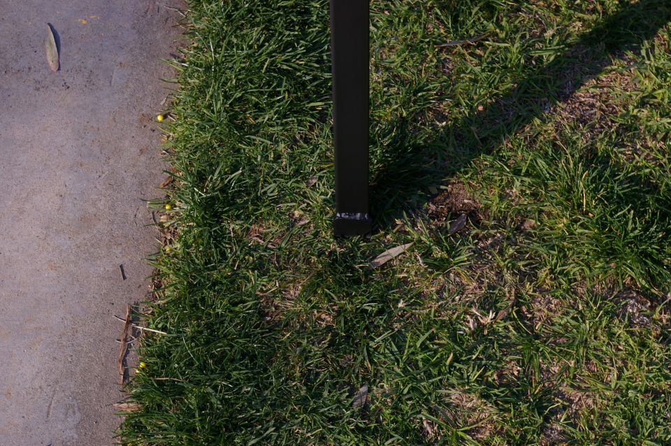 Black metal post on grass next to concrete path