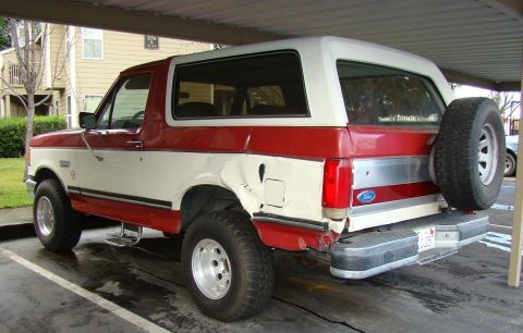 1989 Ford Bronco - This two-tone red and white Ford Bronco features a rear-mounted spare tire and appears to be from the late 1980s.
