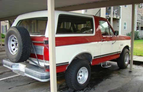 1989 Ford Bronco - This two-tone red and white 1989 Ford Bronco is parked under a carport with a spare tire mounted on the rear.