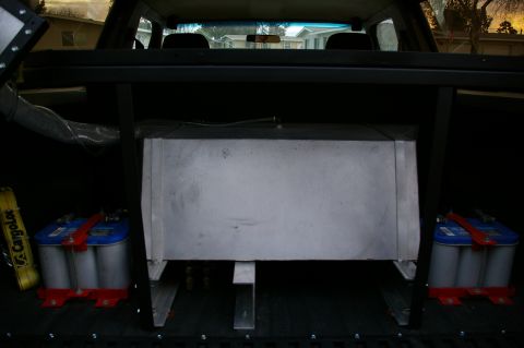 1986 Ford Bronco - View inside a vehicle's cargo area, revealing a large metal tank and two batteries.