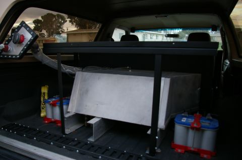1986 Ford Bronco - The interior of a vehicle is shown, a large metal tank and two batteries, along with a custom rack system.