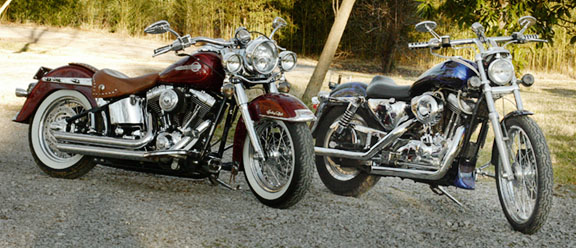 Two motorcycles parked on gravel, one red with a brown seat, the other blue