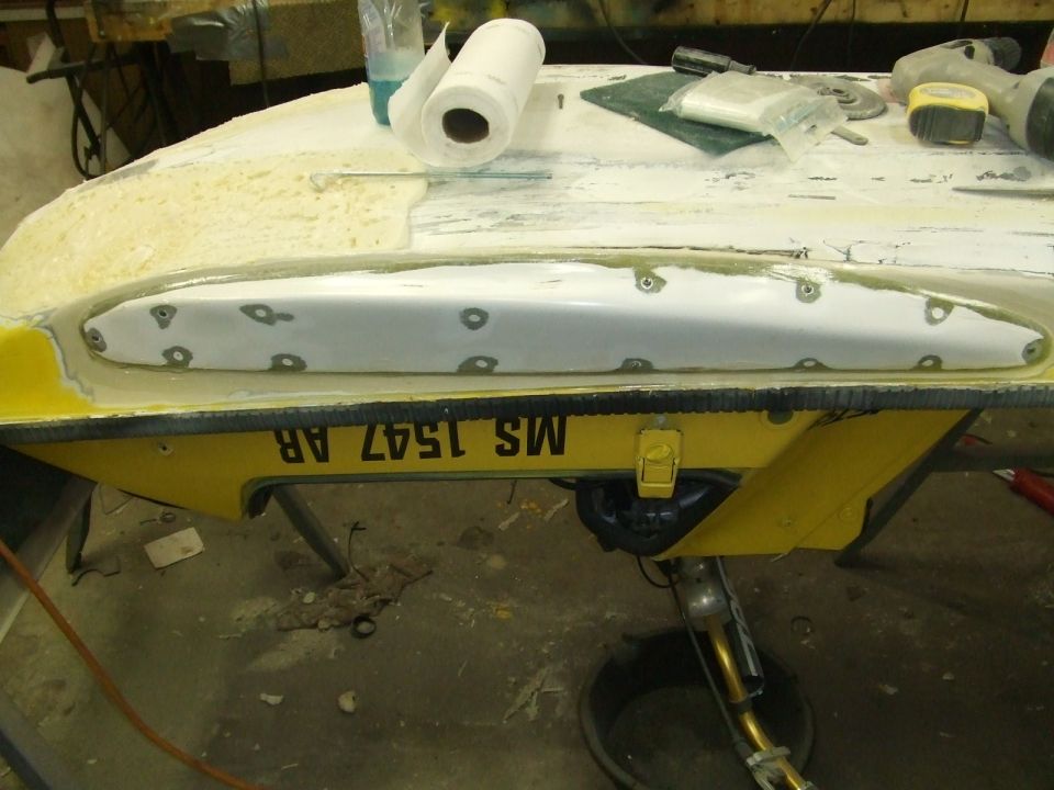 Fiberglass deck repair on a yellow personal watercraft hull in a shop
