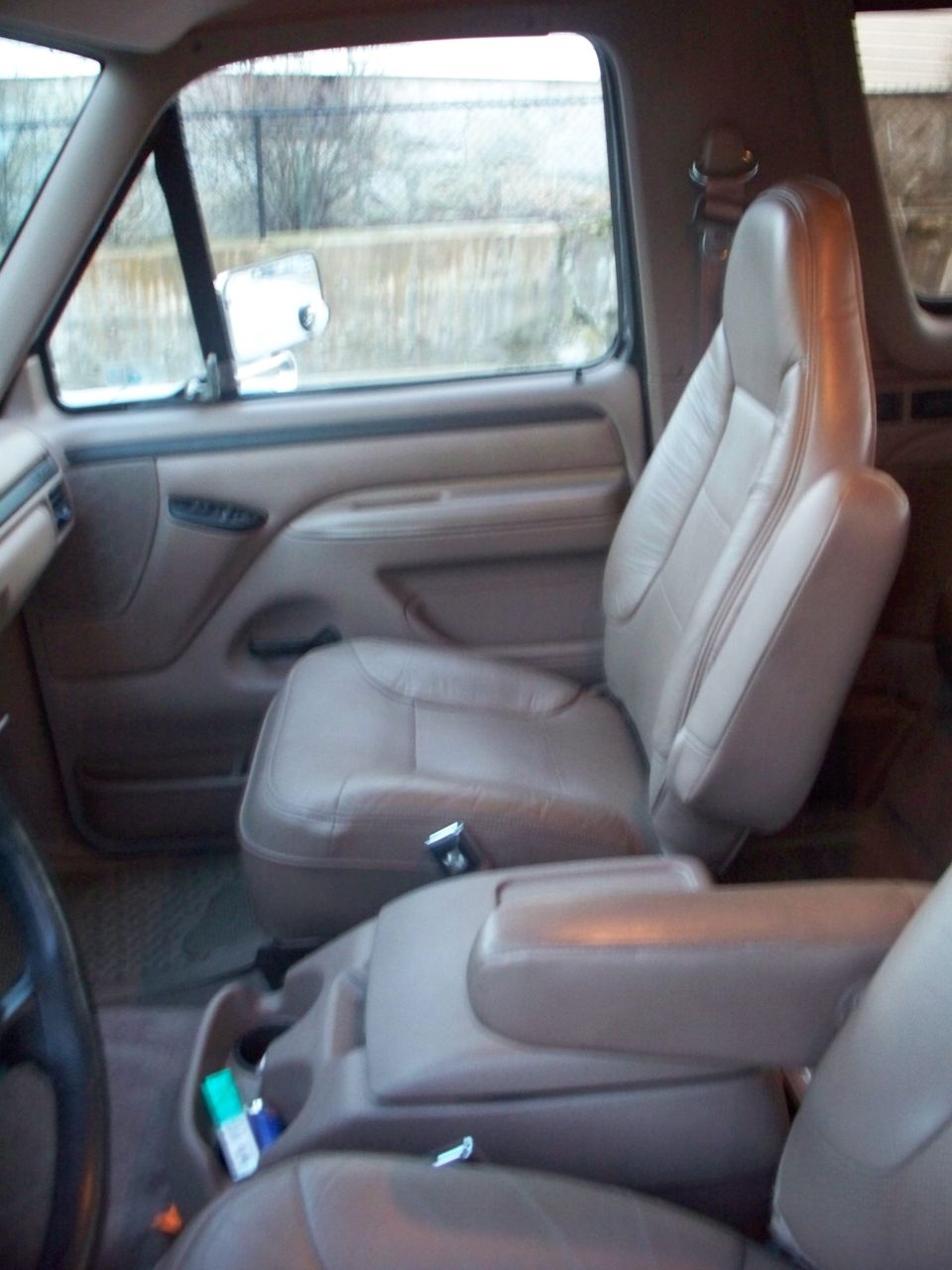 Front seats and center console of a vehicle. Tan leather seats and beige interior panels are visible