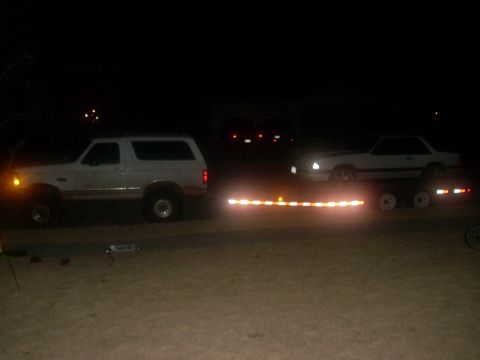 1992 Ford Bronco - A 1992 Ford Bronco is seen from the side at night, towing a car on a trailer.