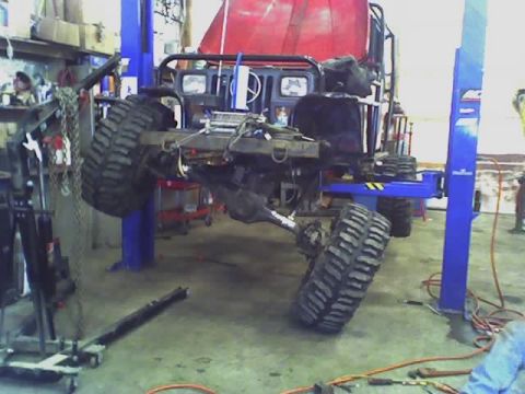 1992 Ford Bronco - The chassis of a heavily modified off-road vehicle is suspended on a lift in a workshop.