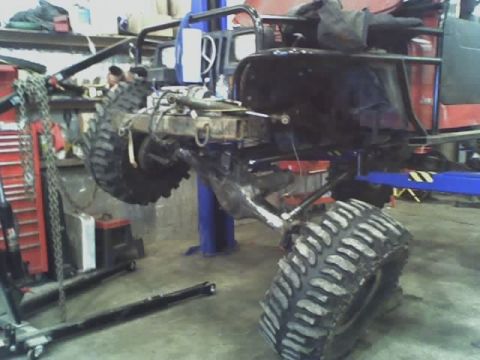 1992 Ford Bronco - The chassis of a red SUV is suspended on a lift, revealing its heavy-duty suspension and oversized tires.