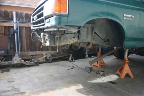 1991 Ford Bronco - Green Ford Bronco front end is disassembled with the bumper removed and suspension components laid out.