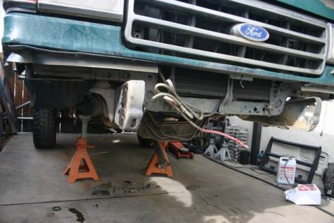 1991 Ford Bronco - Front view of a 1991 Ford Bronco, identified by its badge, undergoing maintenance while raised on jack stands.