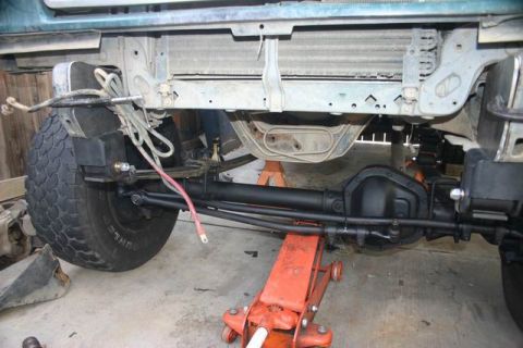 1991 Ford Bronco - The underside of a vehicle is shown with its front axle and suspension components exposed for work.