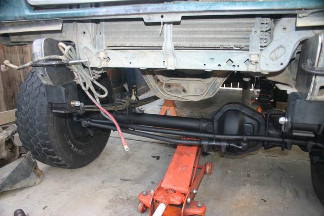 Front axle and suspension parts of a vehicle on jack stands, showing the steering linkage and brake lines