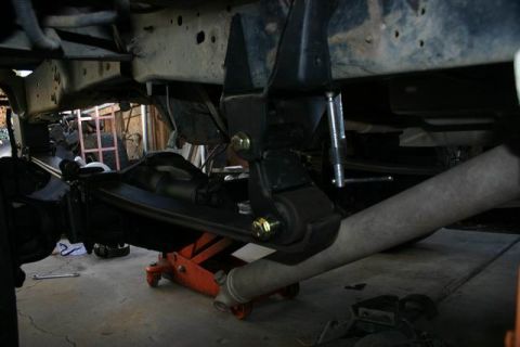 1991 Ford Bronco - Close-up view of a vehicle's leaf spring suspension system being worked on, supported by a jack.