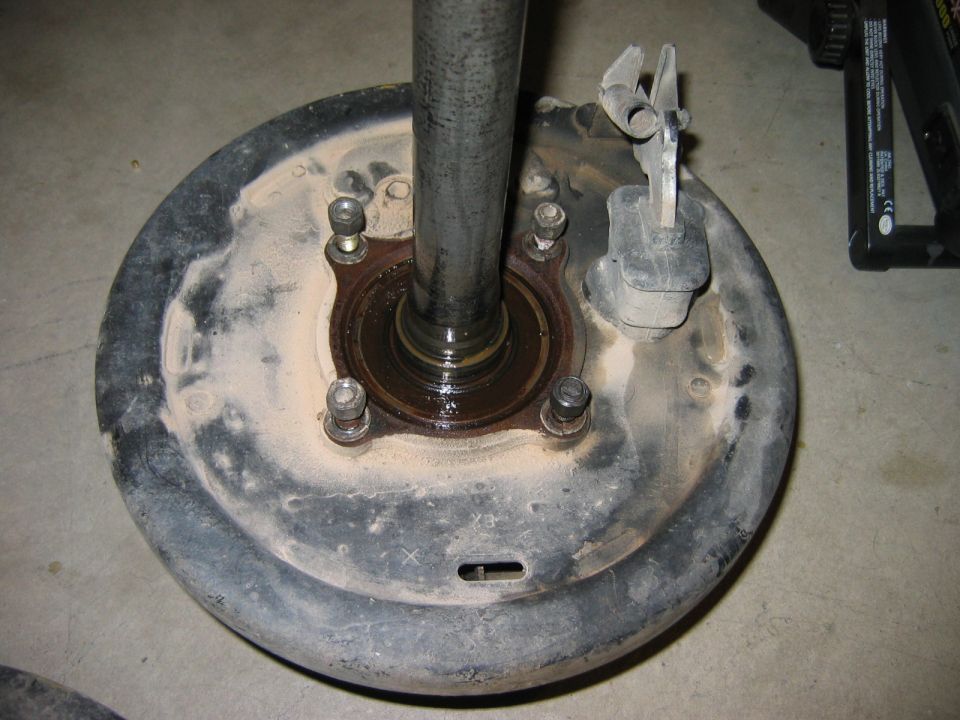 Rear axle hub with brake drum, showing bearing and mounting bolts. A metal shaft extends upwards