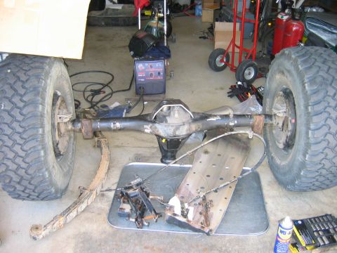 1985 Toyota 4Runner - A rear axle assembly with large tires and leaf springs is shown in a garage setting with a welding machine nearby.
