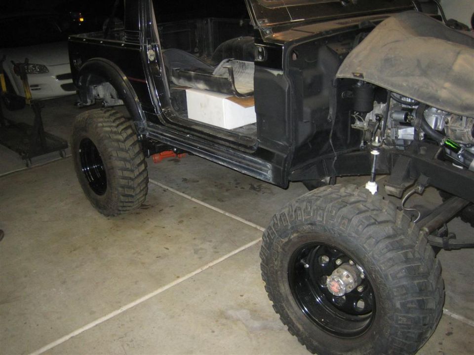 Black off-road vehicle with large tires, doors removed, and engine exposed