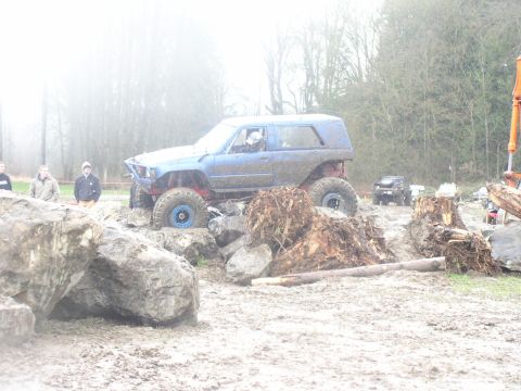 Blue off-road SUV with large tires navigating a muddy obstacle course