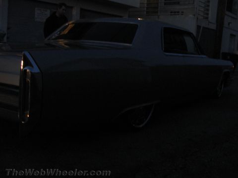 1968 Ford Mustang - A person stands near the rear of a classic Cadillac sedan in dim lighting.