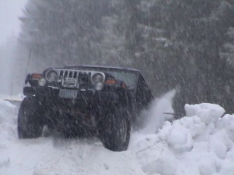 2005 Jeep Wrangler - A black Jeep Wrangler navigates a snowy road, with snow spraying from its tires.