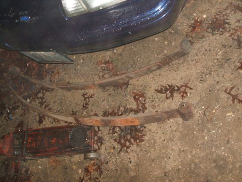 1969 Ford Torino - Two rusty leaf springs lie on the ground next to a car fender and headlight.