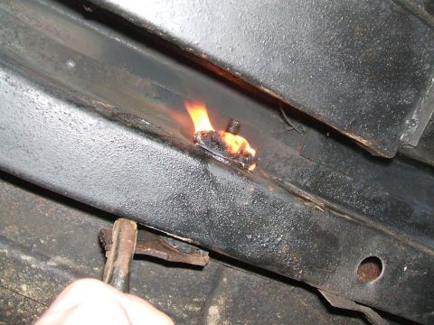 1969 Ford Torino - A bolt on a vehicle's frame rail is heated with a torch, likely during a repair of the rear suspension components.