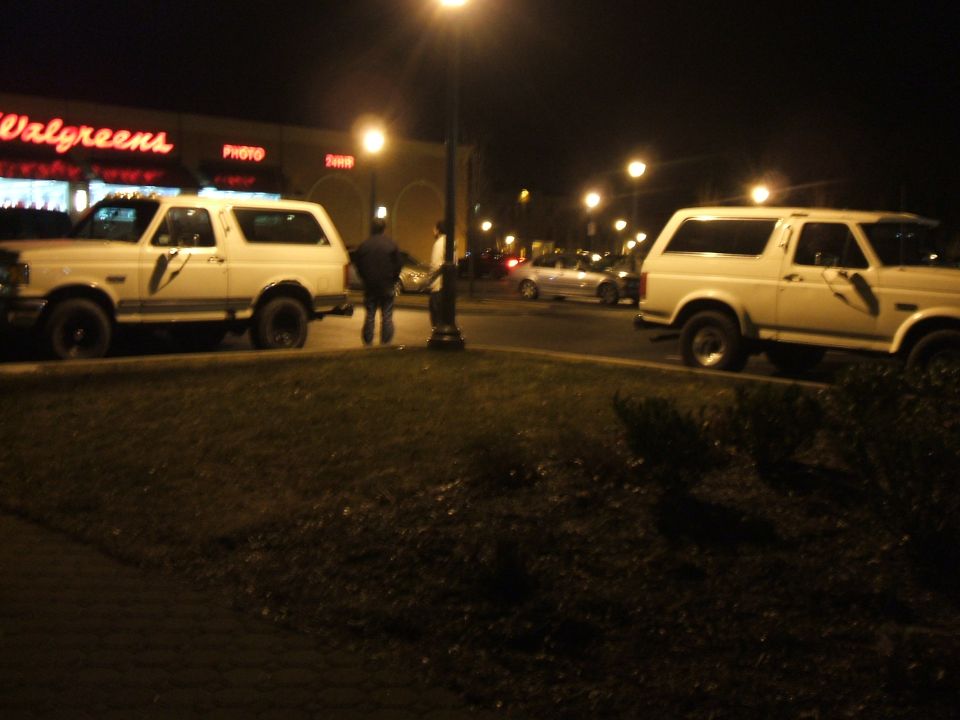 Two white 1990 Ford Broncos parked at night in front of a Walgreens