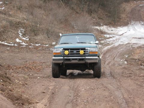 1996 Ford Bronco - 1996 Ford Bronco navigates a challenging dirt road in a wooded area.