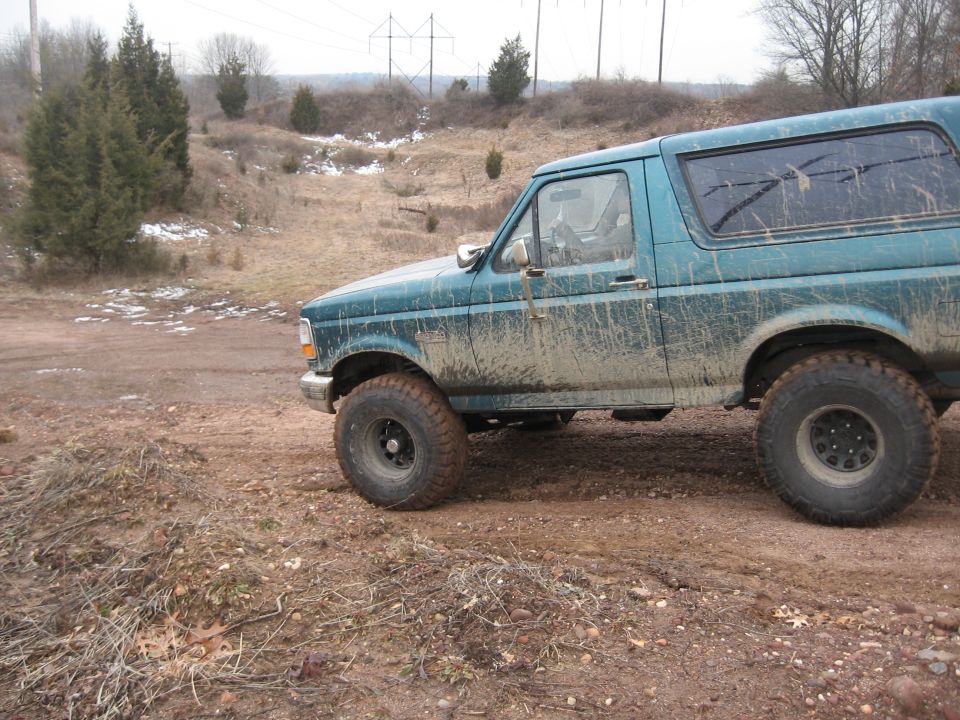 Teal 1996 Ford Bronco side view, covered in mud on a dirt road