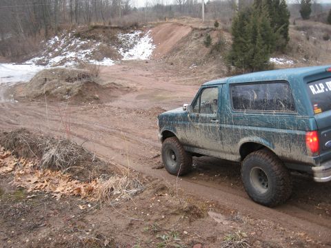 1996 Ford Bronco - Muddy 1996 Ford Bronco navigates a dirt track with snow patches visible in the background.